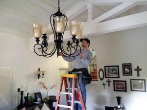 Worker installing a chandelier while standing on a ladder