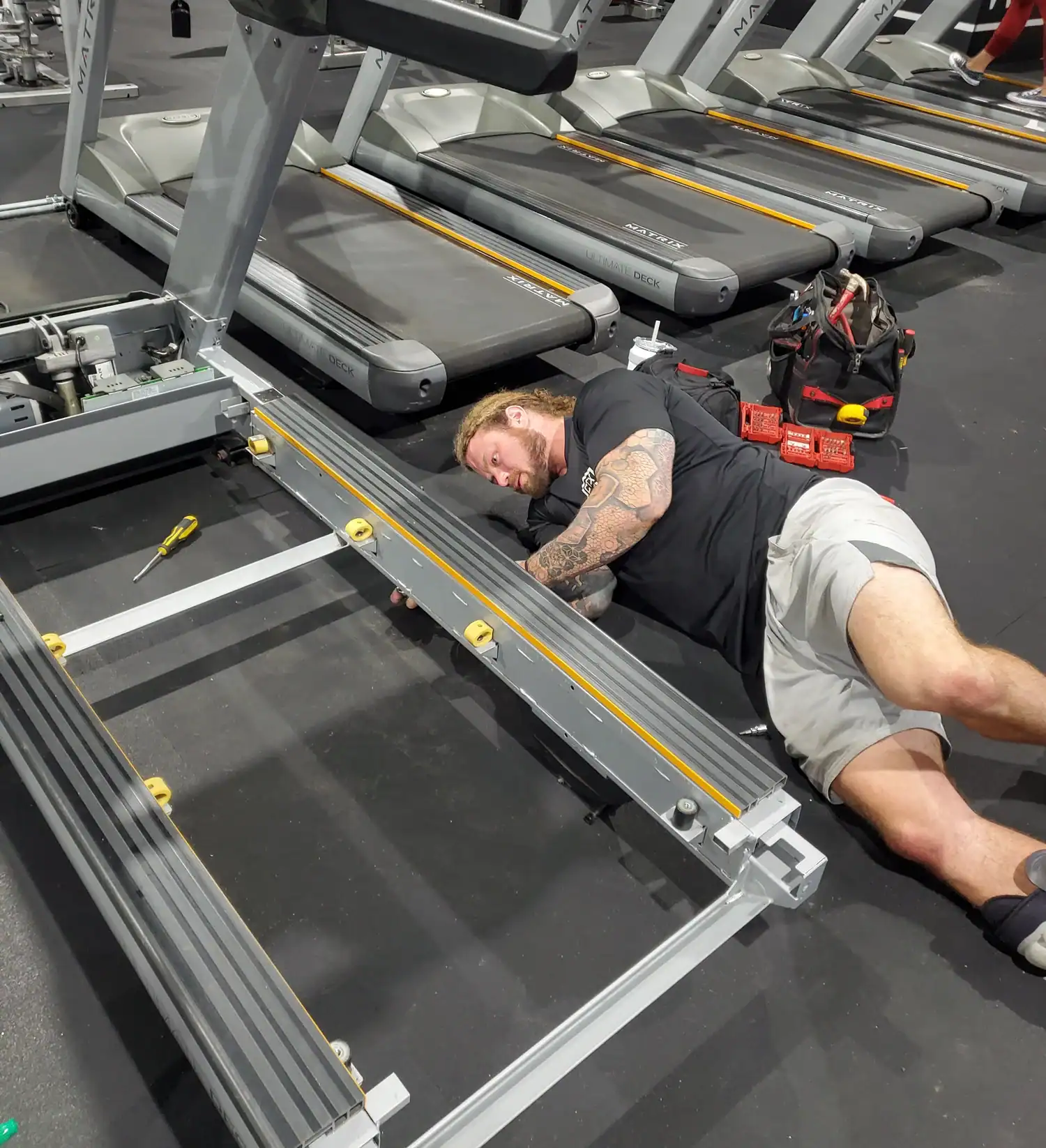Man repairing treadmill at gym, focusing on equipment servicing.